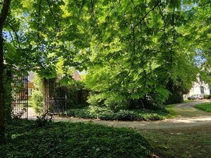 Ein Weg, der durch einen Garten mit dichtem Grün und einem Metalltor führt.