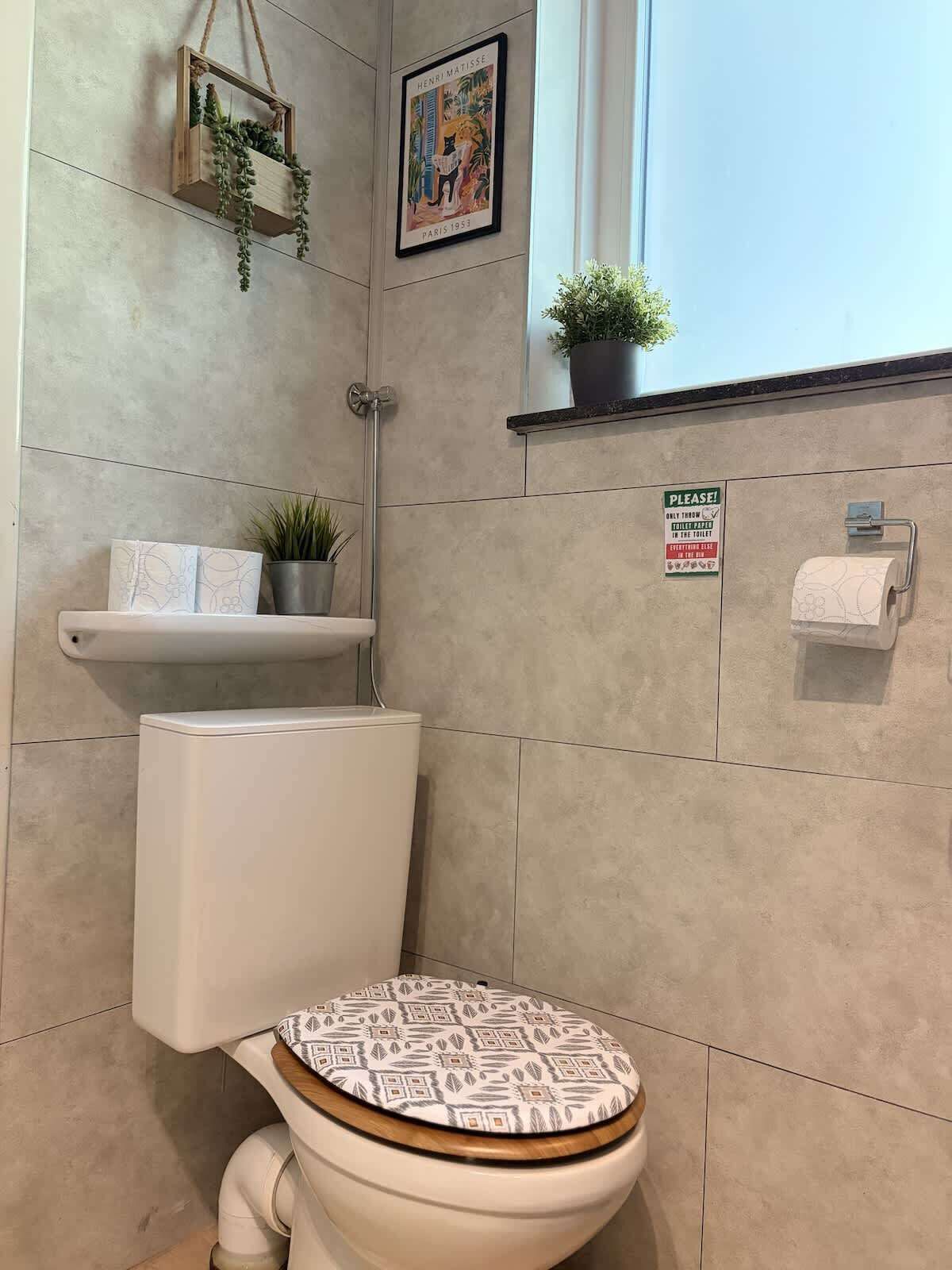 Ein modernes Badezimmer mit Toilette, einer hängenden Pflanze, einem gerahmten Kunstwerk und einem Schild an der Wand.