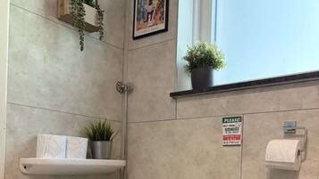 Ein modernes Badezimmer mit Toilette, einer hängenden Pflanze, einem gerahmten Kunstwerk und einem Schild an der Wand.