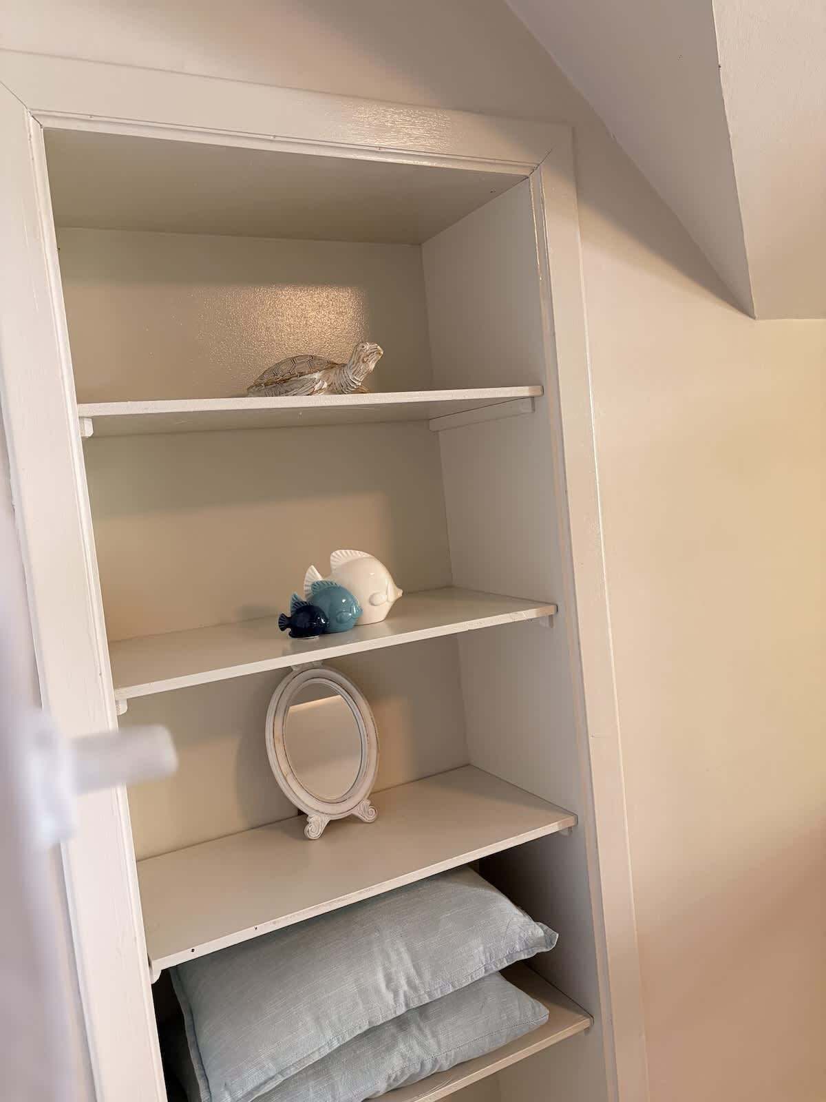 A white shelving unit with decorative items and a mirror.