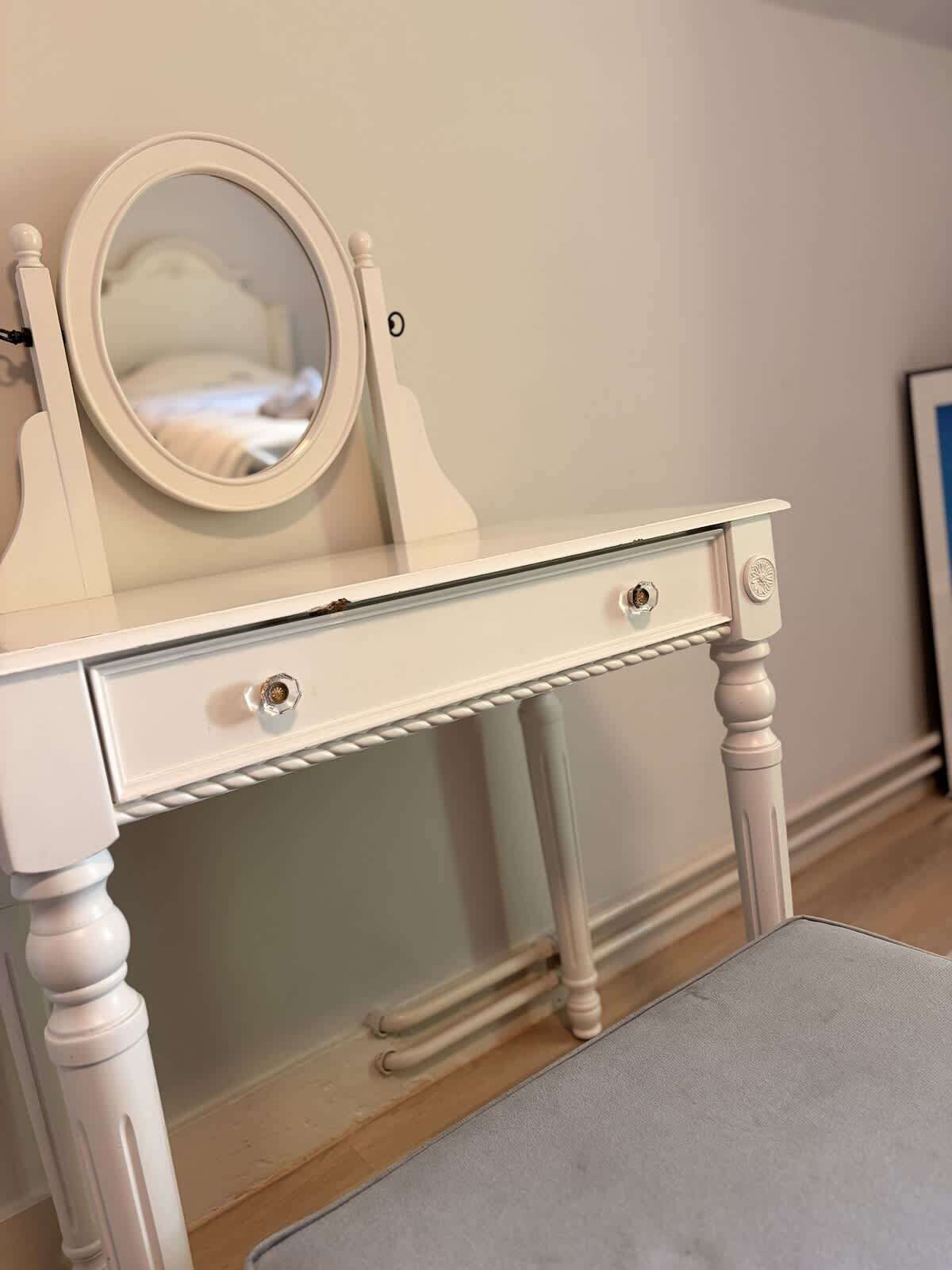 A white vanity with a mirror, two drawers, and a small stool.