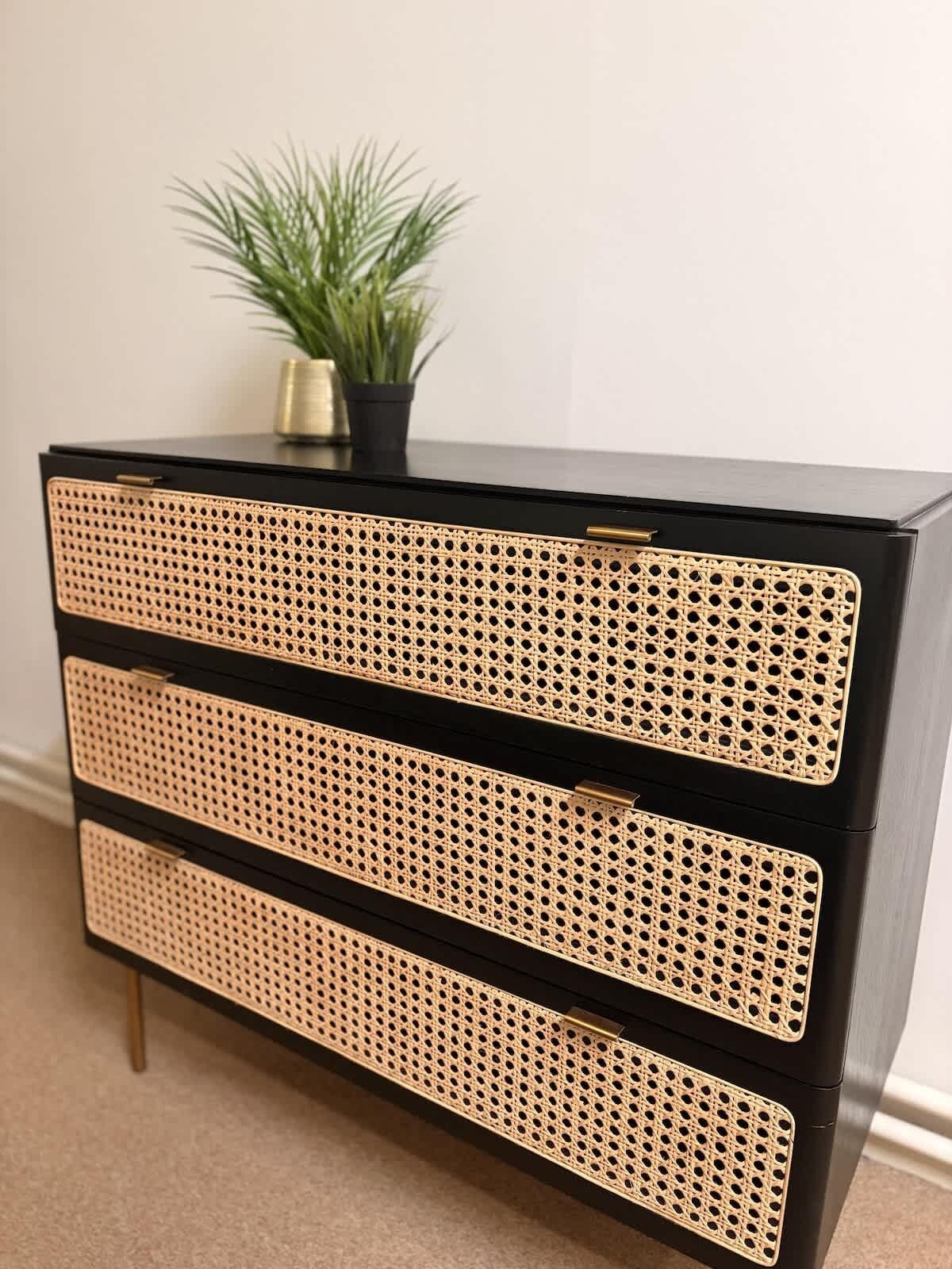 A black dresser with three drawers, each featuring a woven rattan front panel.