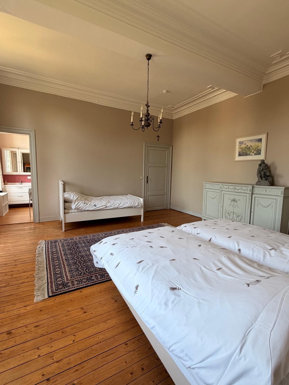 Une chambre à coucher avec un lit double, un lit plus petit, un lustre, une commode et une porte.