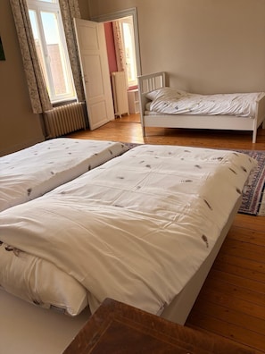 Makuuhuoneessa on kaksi sänkyä, puulattia, patteri ja ikkuna, jossa on verhot.