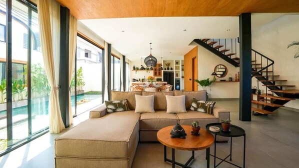 Ein modernes Wohnzimmer mit einer Eckcouch, einem runden Couchtisch und einer Treppe, die zu einer oberen Ebene führt.
