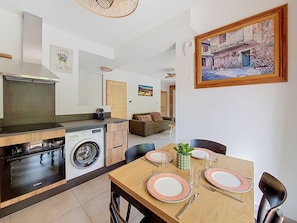 A modern kitchen with Bosch appliances, a dining area with pink plates, and a painting of a rustic building. - Reflets d'Ardent – Sleeps 6 –  Montriond (Montriond)