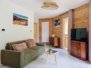 Ein Wohnzimmer mit einer Couch, einem kleinen Tisch mit einer Pflanze, einem Fernseher und Holzwandverkleidung.