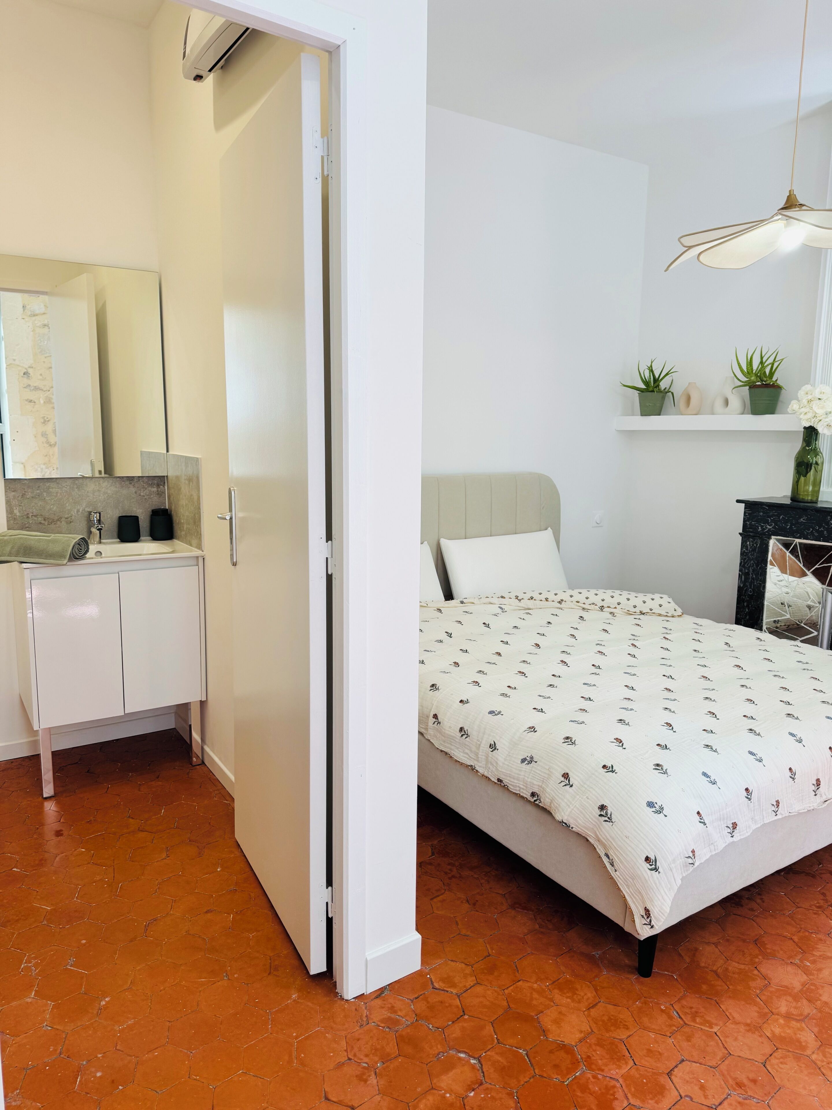 A bedroom with a bed, a nightstand, a dresser, a mirror, and a potted plant.
