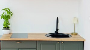 Eine Küche mit grünen Schränken, einer Holzausziehtafel, einem schwarzen Spülbecken, einem Topfpflanzen und einer Lampe.