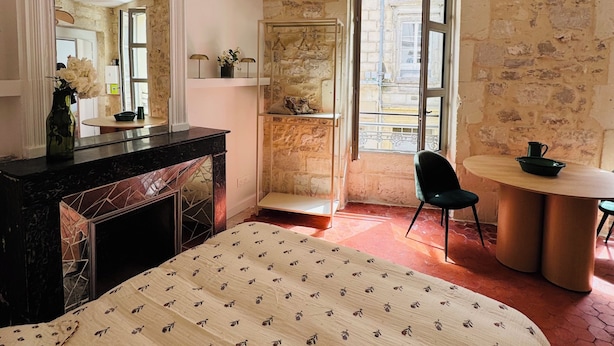 Ein Schlafzimmer mit einem großen Bett, einem Schminktisch, einem Spiegel, einer Hängeleuchte, einer Steinwand und Blick durch ein Fenster.