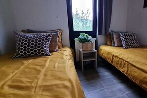 A room with two beds, a small table with a plant, and a window with curtains. - Holiday home in Olburgen with swimming pool (Olburgen)