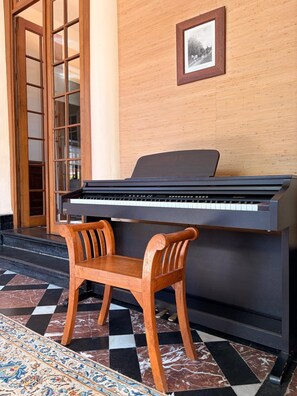 Een vleugelpiano in een kamer met een geruite vloer, een houten stoel en een lijst met een afbeelding erop.