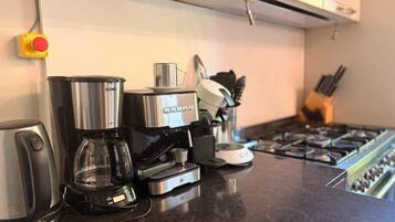 A kitchen with a coffee maker, a kettle, and a stove.