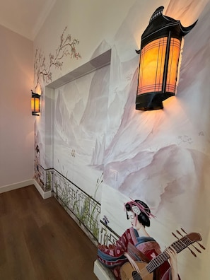 A room with a mural of a mountainous landscape, a traditional Chinese lantern, and a person playing a stringed instrument.