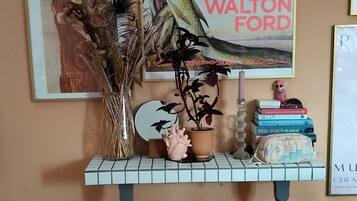 Een kamer met een houten vloer, een grijze vloerkleed, een tafel met een vaas, boeken en lijstwerken aan de muur.