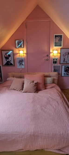 Et soveværelse med skråvæg, en seng med et pink dynebetræk og vægmonterede lamper.