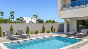 Une piscine rectangulaire dont le bord est recouvert de carreaux, entourée de chaises longues et de petites plantes.