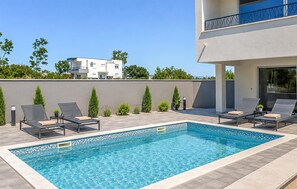 A rectangular swimming pool with a tiled edge, surrounded by lounge chairs and small plants. - Nice home in Privlaka (Privlaka)