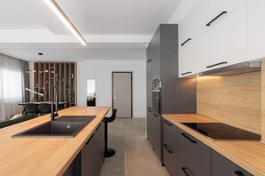 A modern kitchen with a wooden countertop, built-in appliances, and a dining area with a table and chairs. - Oddity Seafront Penthouse Apartments (Thessaloniki)