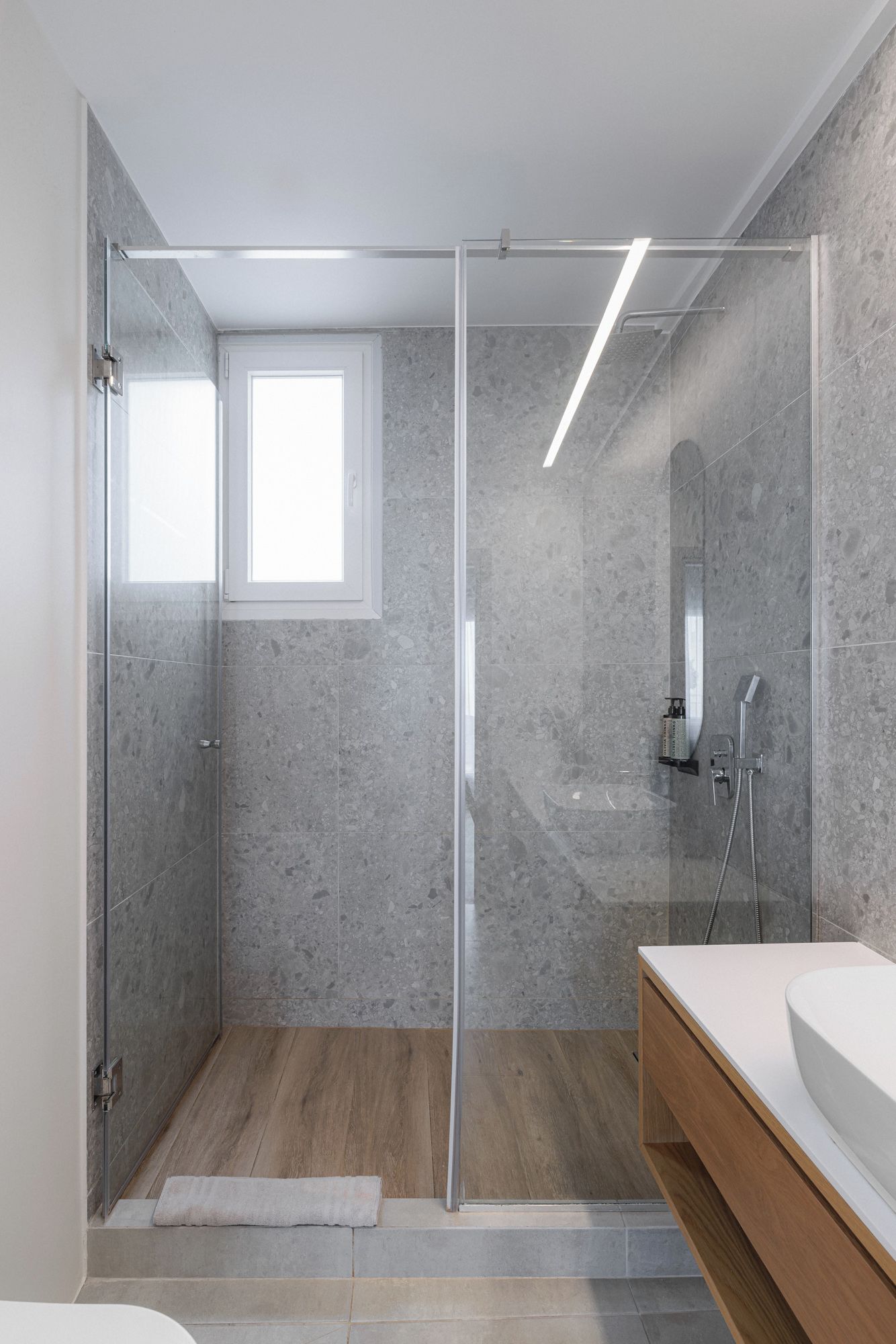 Een moderne badkamer met een douche met glazen wand, een houten wastafelmeubel en een grote spiegel.