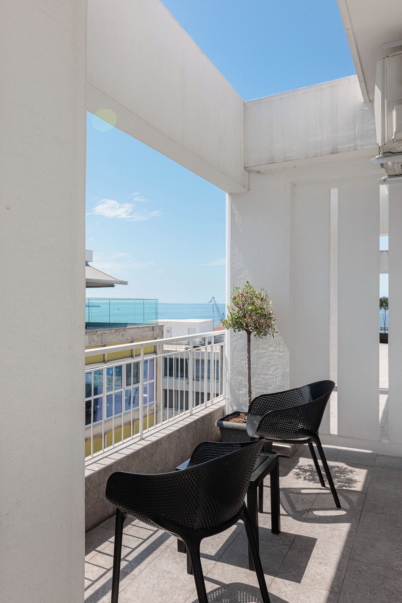 A balcony with two chairs and a small table, overlooking a body of water and a bridge.