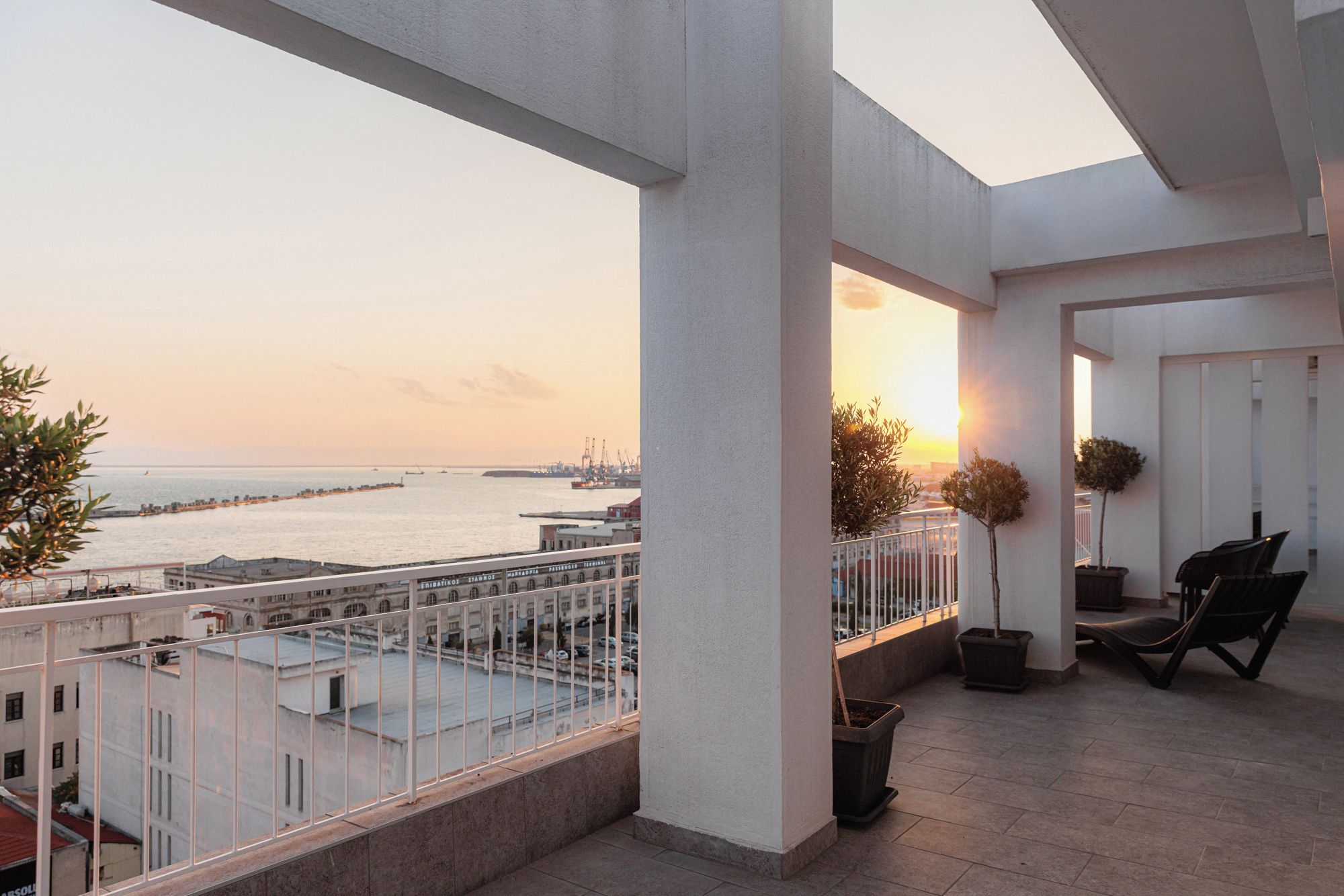 Un balcon avec vue sur la mer et le port, agrémenté d’une balustrade, de plantes en pot et d’une chaise.