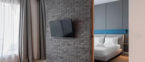 Quarto de hotel moderno com parede de tijolos, TV de tela plana fixada nela, cama com roupa de cama branca e detalhe azul no encosto.