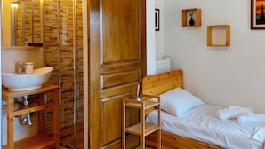 A wooden room with a bed, a wooden chair, a wooden cabinet with a sink, and a wall with framed pictures. - Oddity Seafront Penthouse Apartments (Thessaloniki)