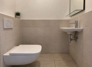 Un baño moderno con inodoro, lavamanos y una pequeña planta en maceta.