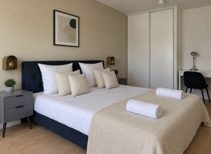 Ein ordentlich eingerichtetes Schlafzimmer mit einem Bett, Nachttischen, einem Schreibtisch und einem Sessel.