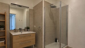 A modern bathroom with a glass-enclosed shower, a wooden vanity with a mirror, and a small shelf with toiletries. - Magnifique 2 pieces a Issy lesMoulineaux (Vanves)