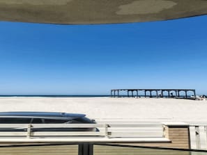 Ein Strand mit einer überdachten Konstruktion und einem Auto im Vordergrund.