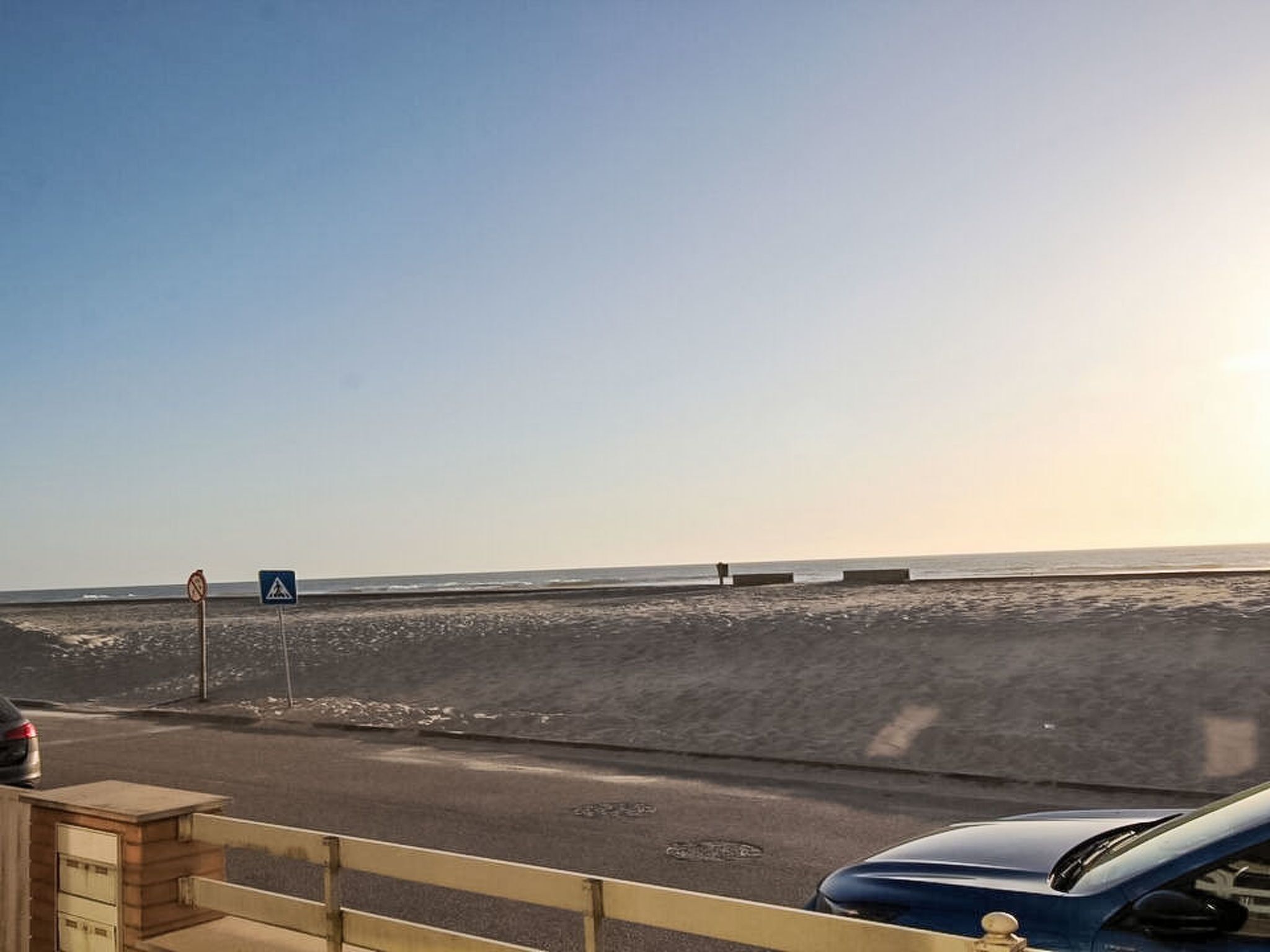 Una carretera costera con una señal de paso para peatones, un coche aparcado y un banco a lo largo de la playa.