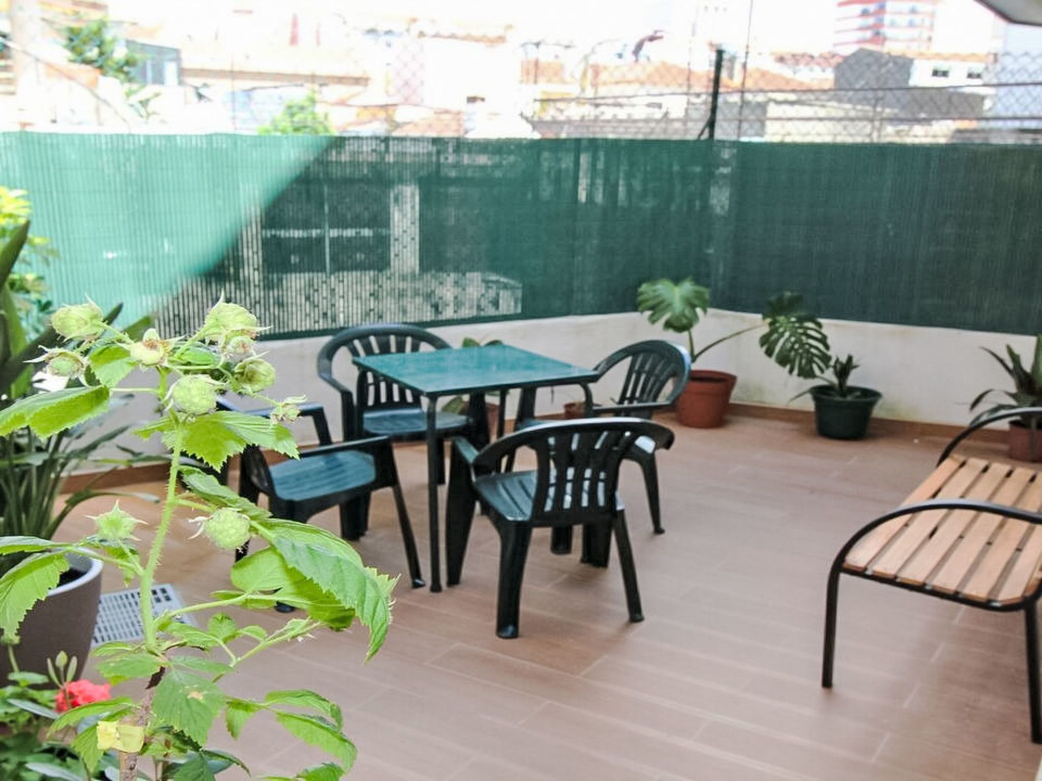 A patio with a table and chairs, potted plants, and a green fence.