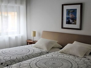 A hotel room with two beds, a bedside table with a lamp, a framed picture on the wall, and sheer curtains on the window. - Aveiro Apartment with Patio by Interhome (Aveiro)