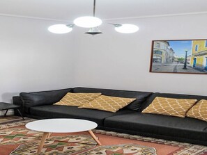 A living room with a black sofa, patterned cushions, a white coffee table, and a painting of a street scene on the wall. - Aveiro Apartment with Patio by Interhome (Aveiro)