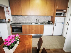 A compact kitchen with wooden cabinets, a gas stove, a microwave, and a dishwasher. - Aveiro Apartment with Patio by Interhome (Aveiro)