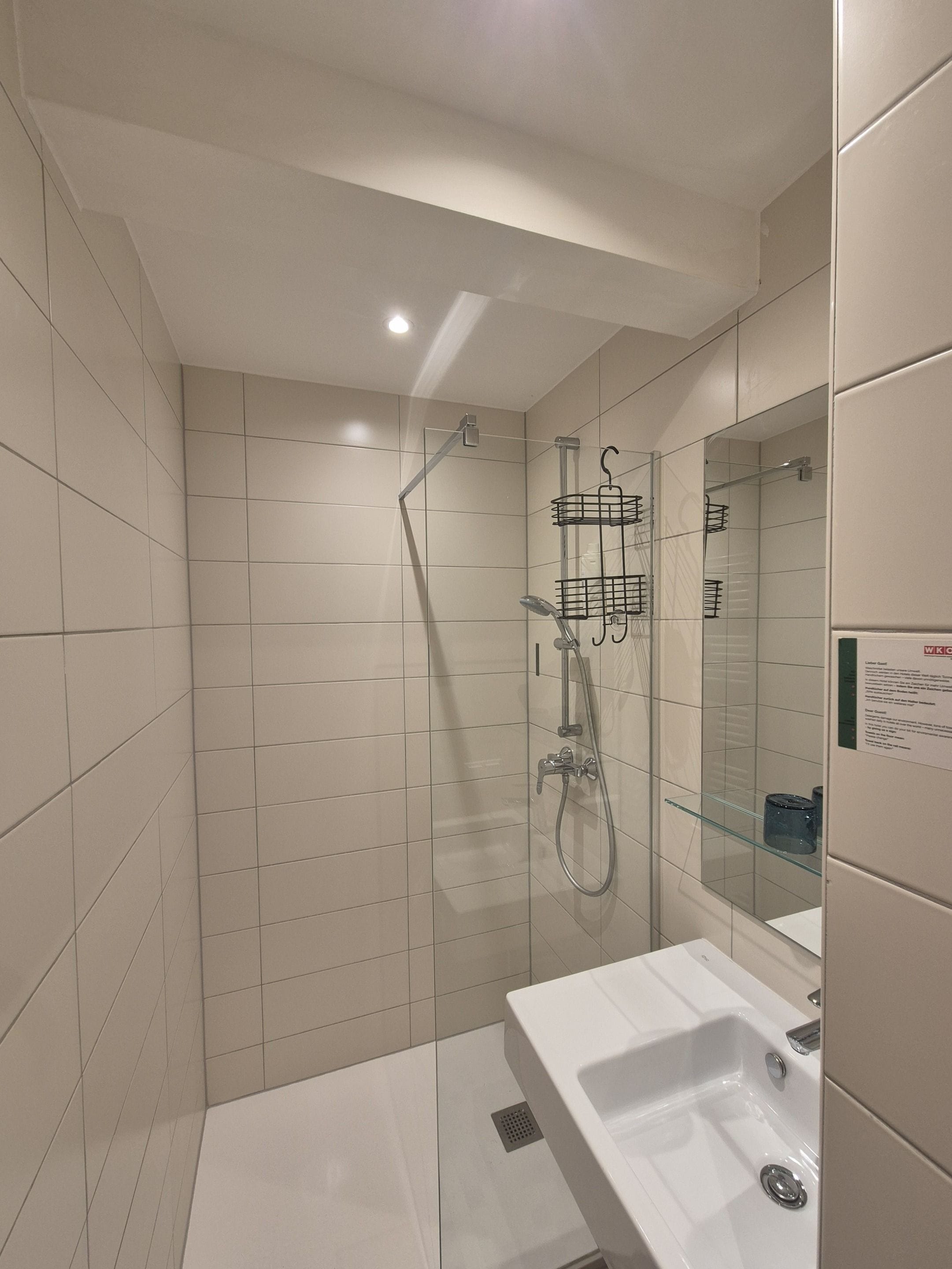 A modern bathroom with a glass shower enclosure, a white sink, and a mirror with a sign.