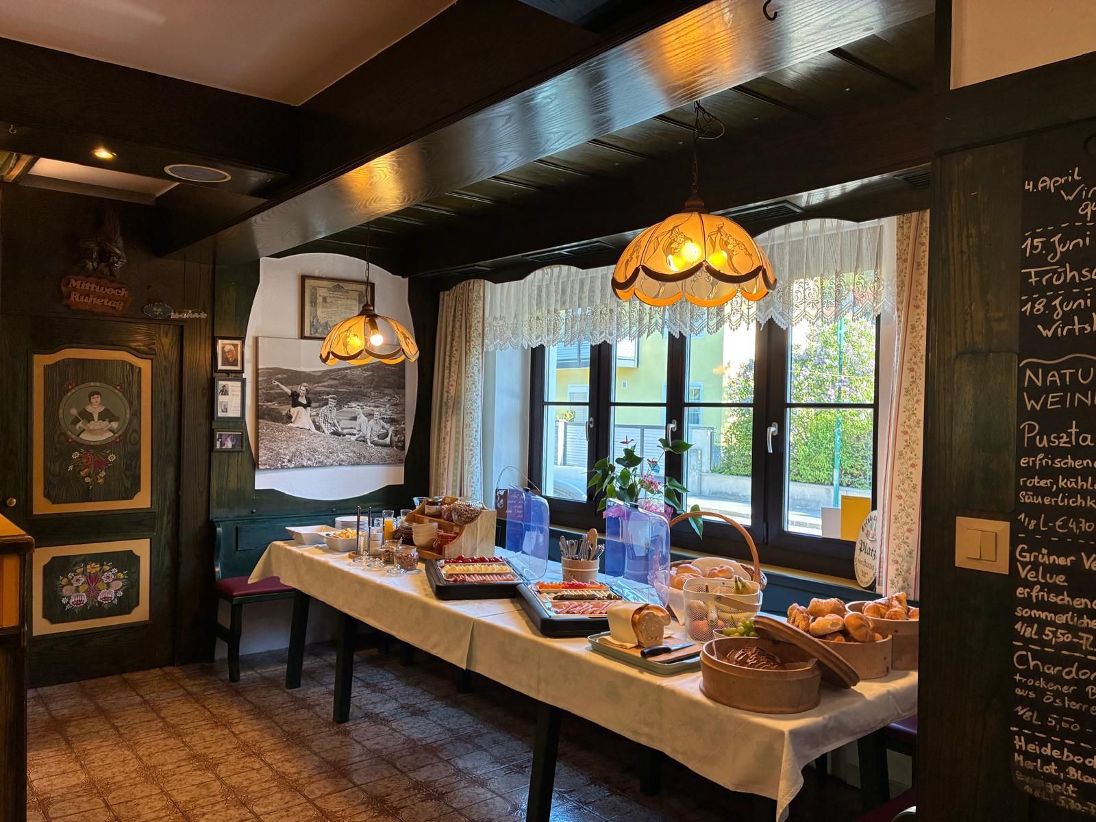 Un comedor con una mesa larga dispuesta para una comida, un menú en una pizarra y una ventana con cortinas.