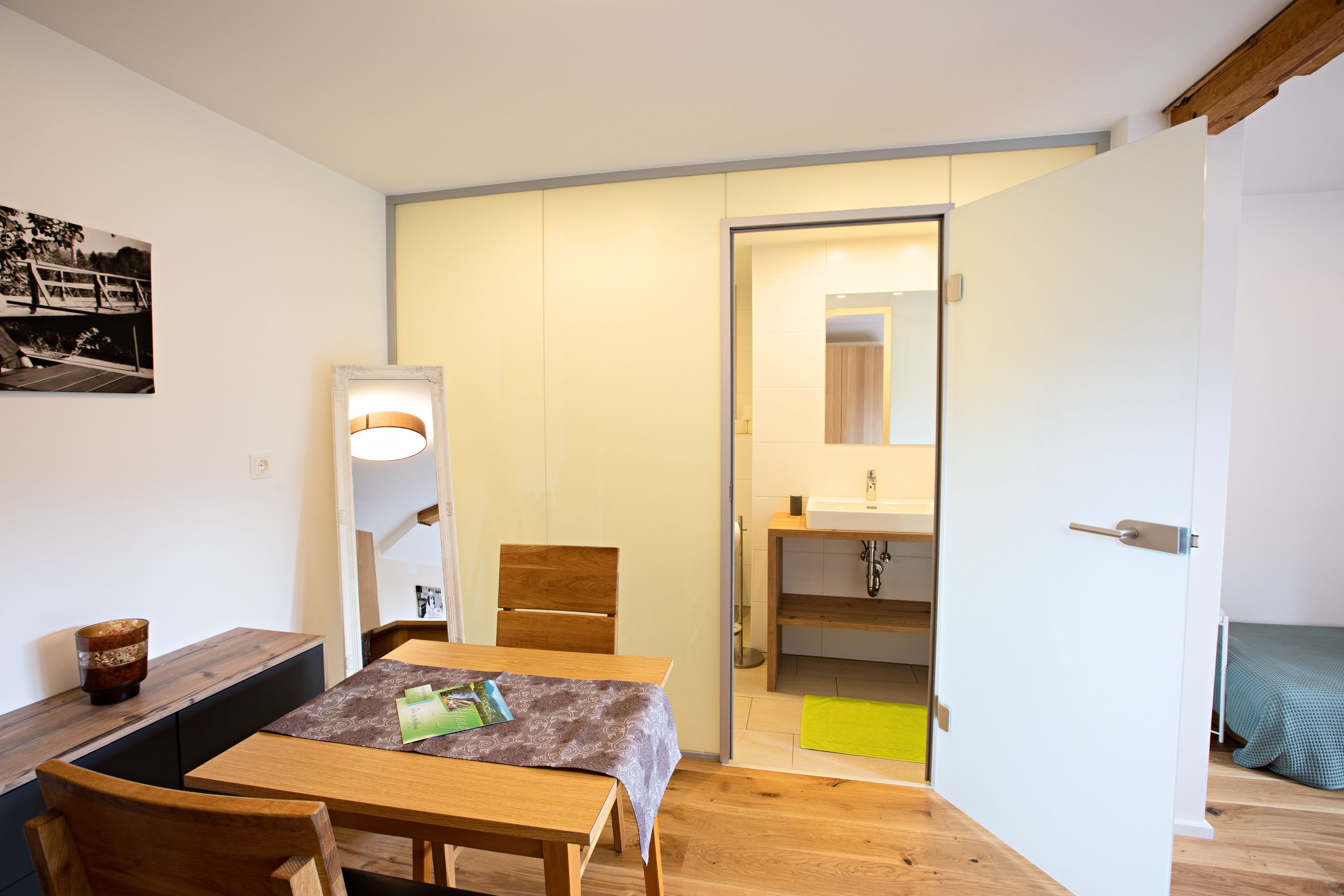 Une pièce de taille modeste comprenant une table à manger, des chaises, un miroir et une petite salle de bain avec un lavabo.