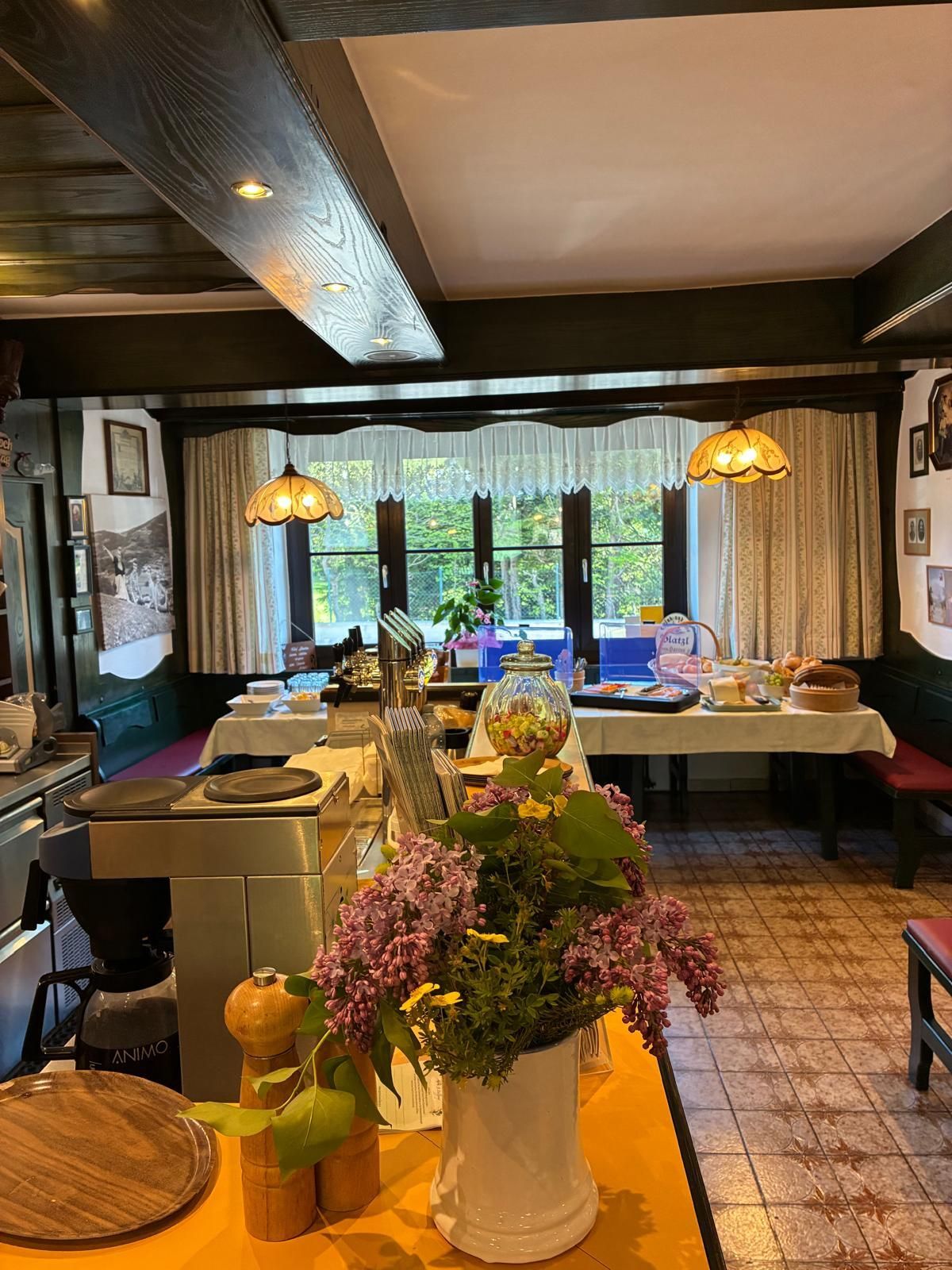 Un comedor con una mesa lista para una comida, una cafetera y una ventana con cortinas.