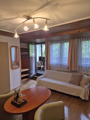 Una habitación acogedora con piso de madera, un sofá, una mesa de comedor con botellas y una lámpara en el techo.