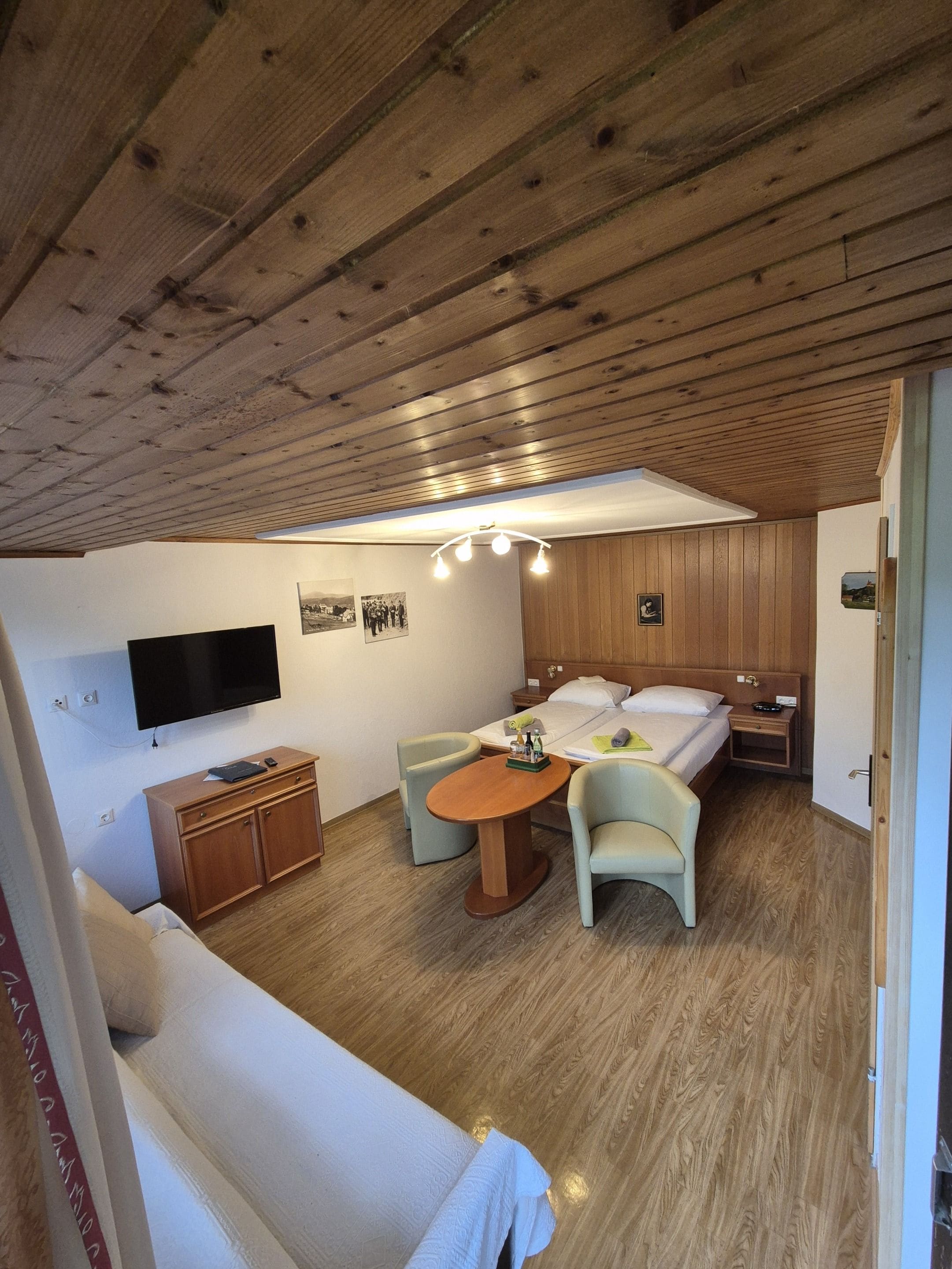 Une pièce de taille modeste comprenant un lit, un bureau, une chaise, un téléviseur et une petite table.