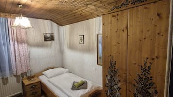 Ein Zimmer mit Holzboden, einem Bett, einem Nachttisch, einem Kleiderschrank und einem Deckenventilator.
