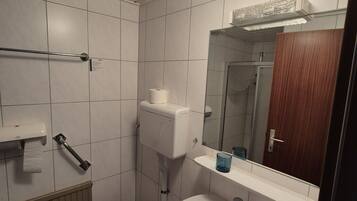 Baño con inodoro, lavamanos, espejo y dispensador de toallas.