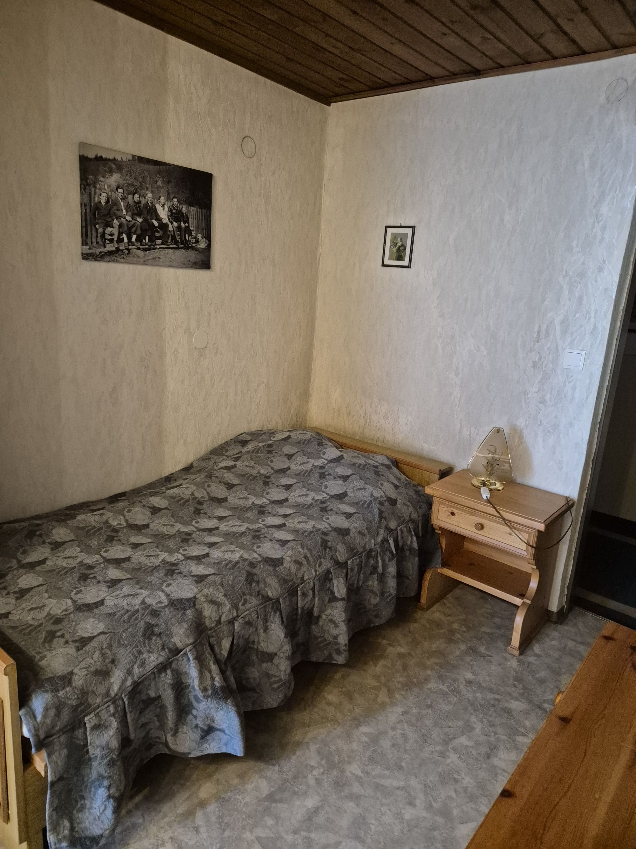 A bedroom with a single bed, a small wooden nightstand, and a wall-mounted picture.