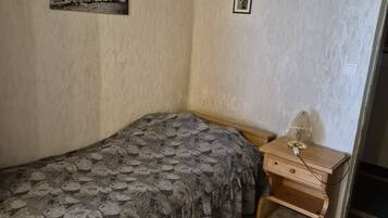 A bedroom with a single bed, a small wooden nightstand, and a wall-mounted picture.