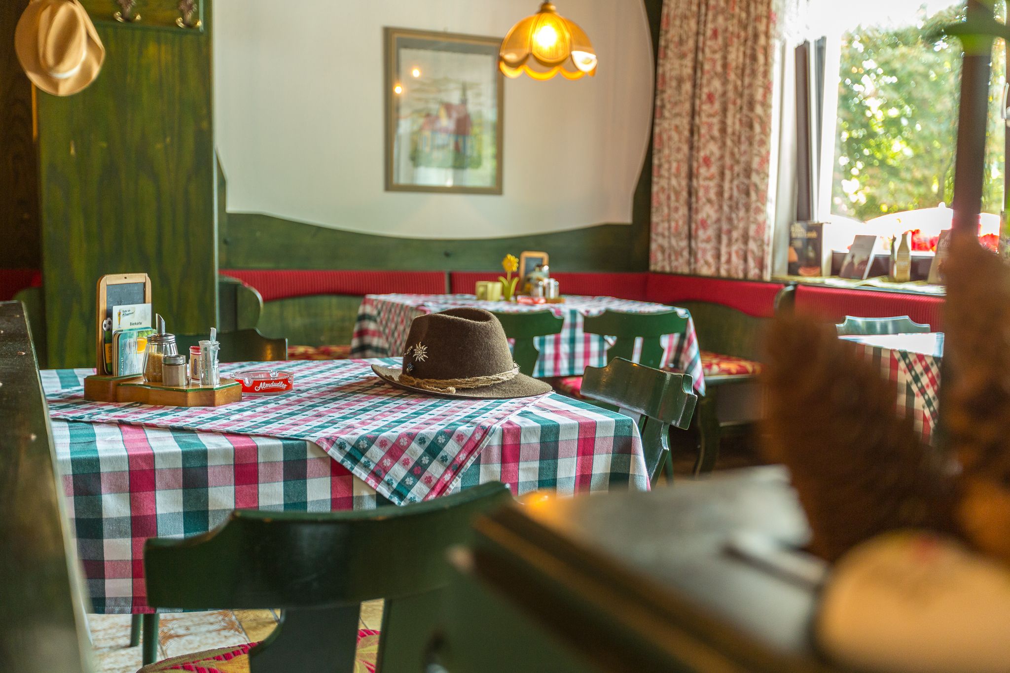 A restaurant interior with checkered tablecloths, a hat on a table, and a hanging light fixture.