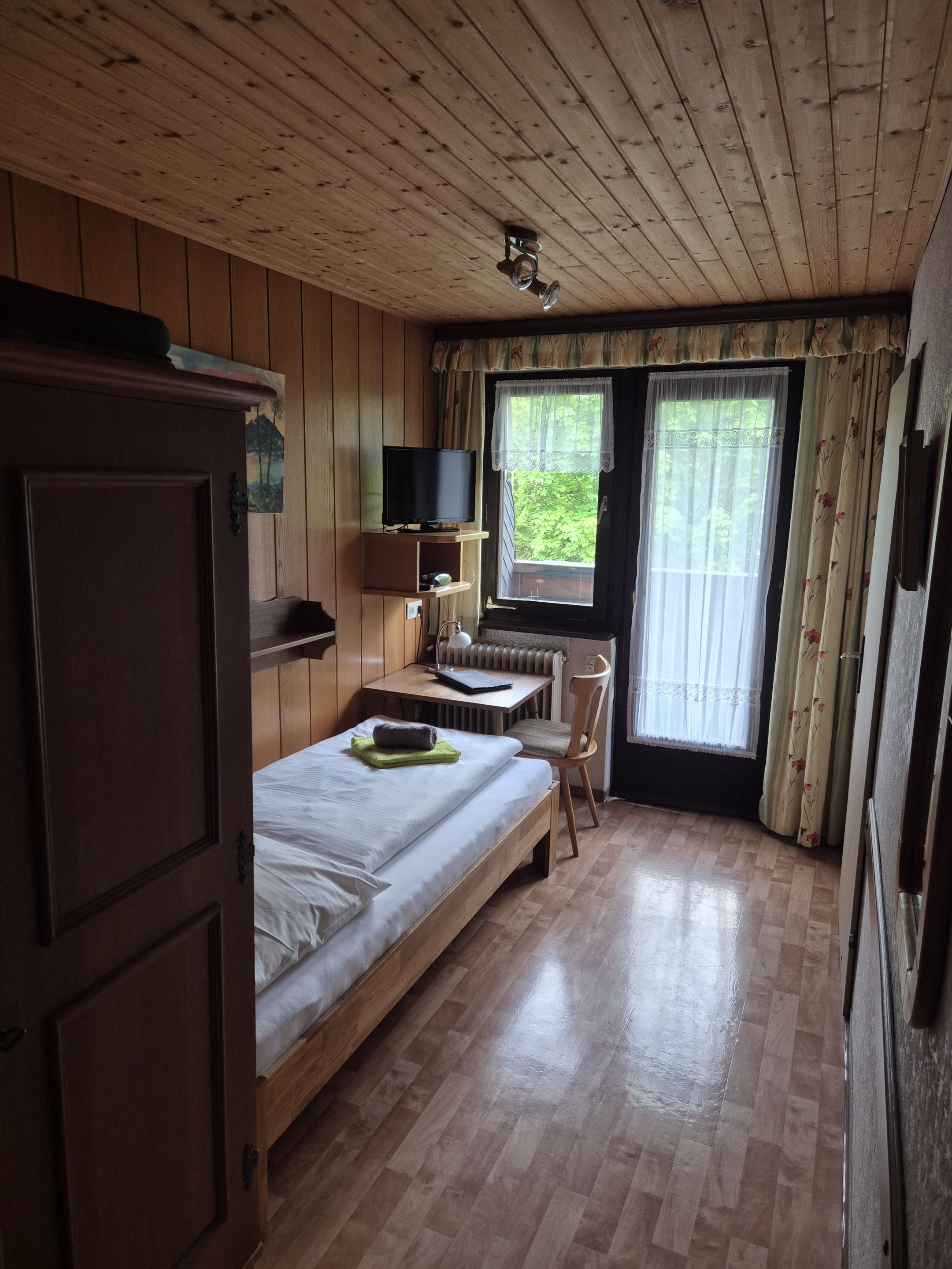 A wooden-paneled room with a bed, a desk, a chair, and a television.