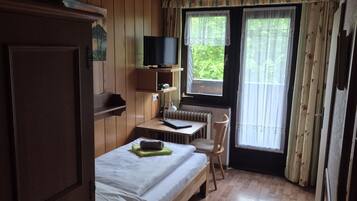 A wooden-paneled room with a bed, a desk, a chair, and a television.